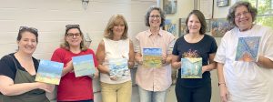 art students of Anne Stine hold up their paintings in a workshop